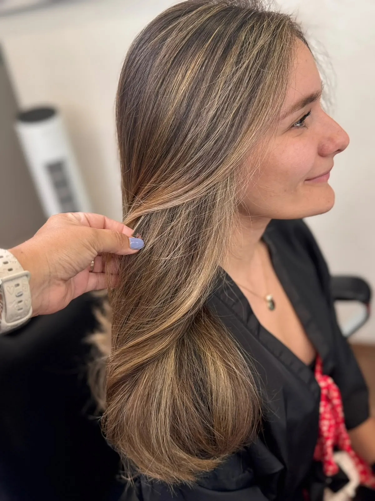 Melena larga castaña con balayage rubio, peinada de lado, en un salón con luz natural.