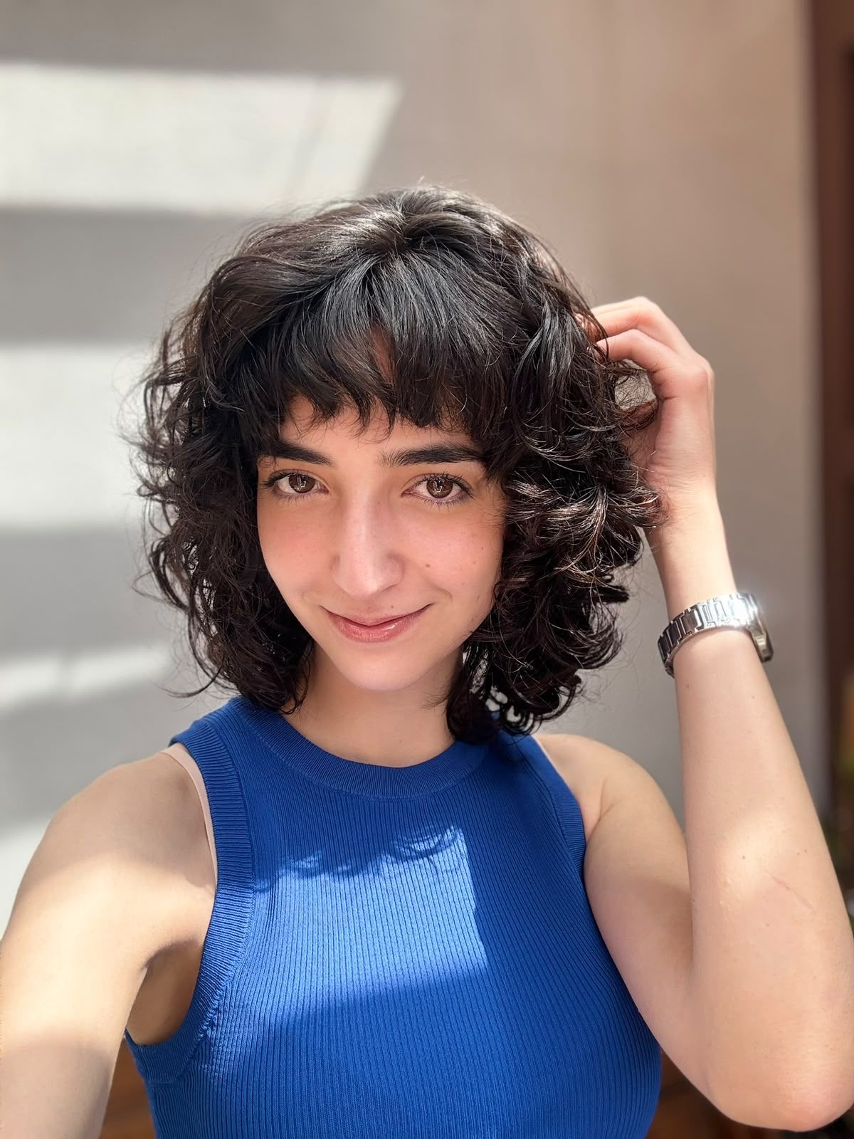 Corte de melena rizada con flequillo, peinado con luz natural.